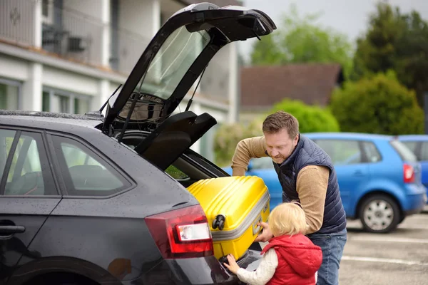 ハンサムな男と彼の小さな息子は、車のトランクに彼らのスーツケースをロードし、休暇に行きます。田舎の自動車旅行。子供と家族のためのロードトリップ — ストック写真