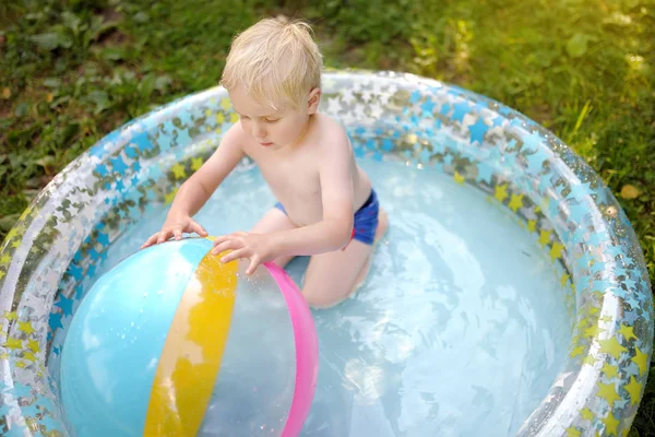 Carino bambino che nuota in una piscina gonfiabile all'aperto sul cortile nella soleggiata giornata estiva . — Foto Stock