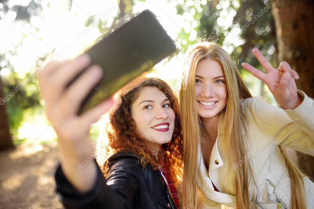 Two beautiful young women take selfie on sunny park. Girlfriends.