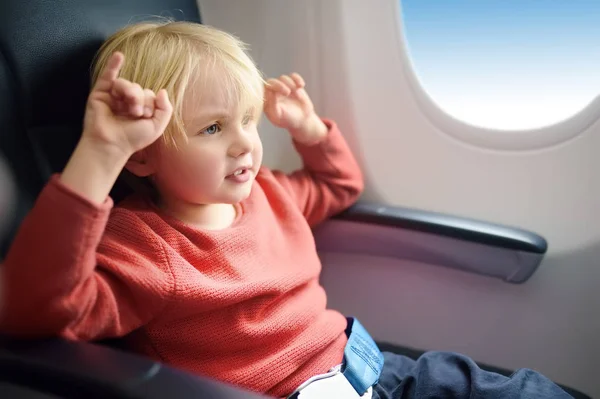 Un chico encantador viajando en un avión. Niño sentado junto a la ventana del avión durante el vuelo. Viajes aéreos con niños . — Foto de Stock