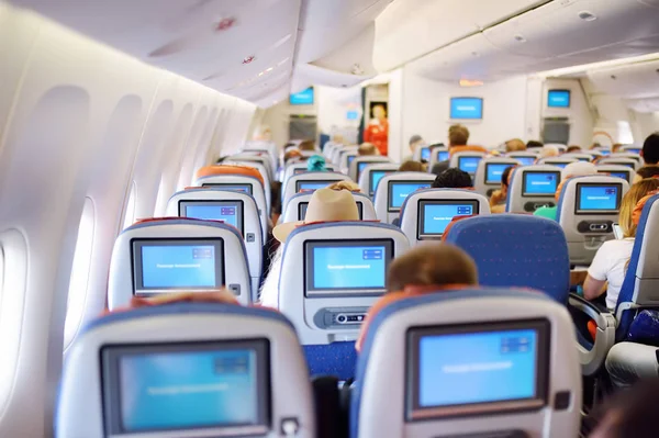 Pasajeros que viajan en un avión comercial sentado en la silla. Azafata de pie en el pasillo entre las filas en el salón del avión . — Foto de Stock