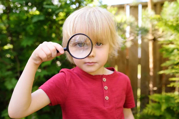 Little boy playing with magnifying glass. Little boy carefully looking at you with magnifier — Stock Photo, Image