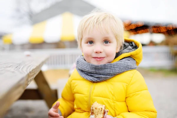 Ragazzino che pranza dopo aver fatto shopping sul mercato agricolo tradizionale in autunno. Bambino mangiare ciambelle . — Foto Stock