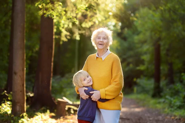 Nieto cariñoso abrazando tiernamente a su jubilosa abuela anciana durante el paseo en el parque de verano . — Foto de Stock