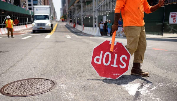 Nova York, EUA - 9 de julho de 2019: Trabalhador rodoviário negro carrega um sinal de parada em uma rua da cidade de Nova York. Ele pára o movimento durante a construção . — Fotografia de Stock