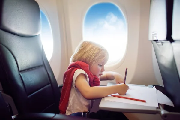 Un chico encantador viajando en un avión. Niño alegre sentado junto a la ventana del avión durante el vuelo. Dibujo infantil . — Foto de Stock