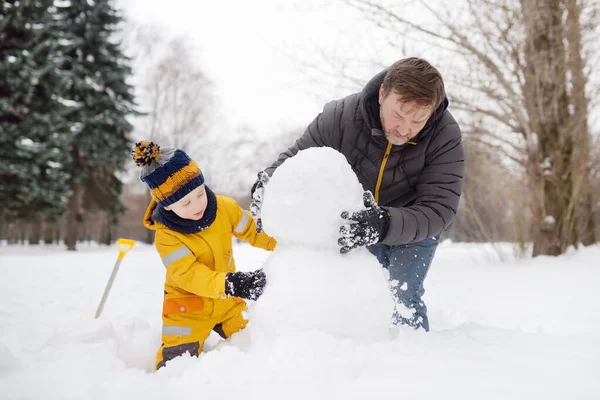 Petit garçon avec son père construisant bonhomme de neige dans un parc enneigé. Loisirs en plein air actifs avec enfants en hiver . — Photo