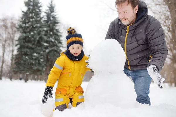 Kleine jongen met zijn vader die sneeuwpop bouwt in het snowy park. Actief buitenrecreatie met kinderen in de winter. — Stockfoto