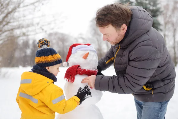 Kleiner Junge mit seinem Vater beim Schneemannbauen im verschneiten Park. Aktive Freizeit im Freien mit Kindern im Winter. — Stockfoto