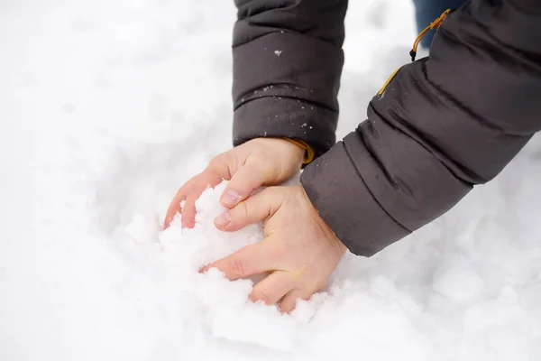 男は雪玉を作っている。冬の楽しみ手を閉じて. — ストック写真