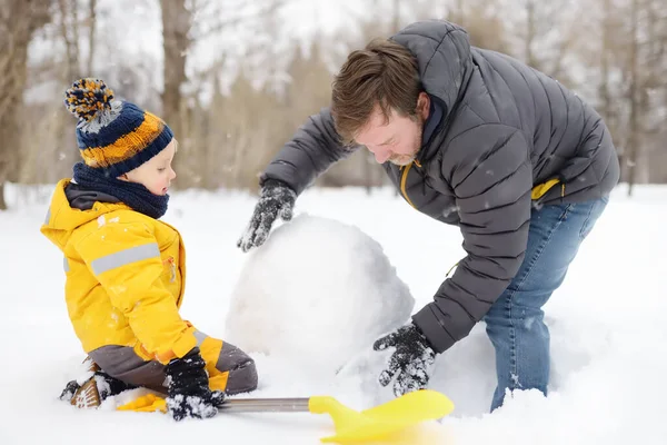 Kleiner Junge mit seinem Vater beim Schneemannbauen im verschneiten Park. Aktive Freizeit im Freien mit Kindern im Winter. — Stockfoto