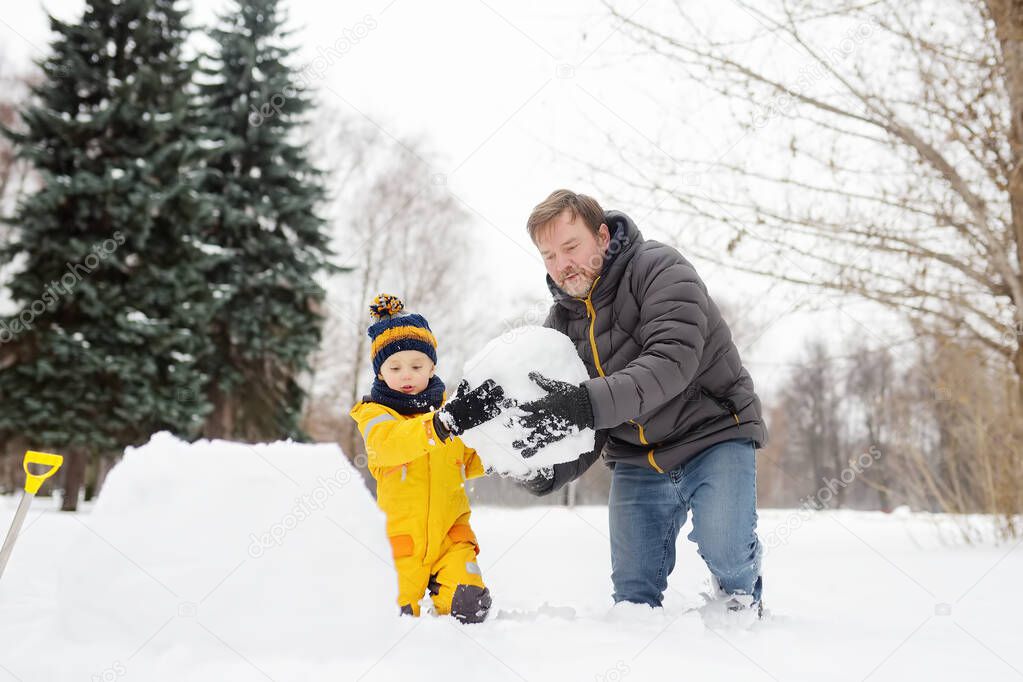 Little boy with his father building snowman in snowy park. Active outdoors leisure with children in winter.