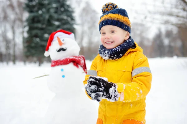 Little boy playing with funny snowman. Active outdoors leisure with children in winter. — Stock Photo, Image