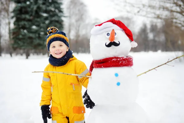 小男孩和有趣的雪人一起玩。 冬季与儿童一起积极参加户外活动. — 图库照片