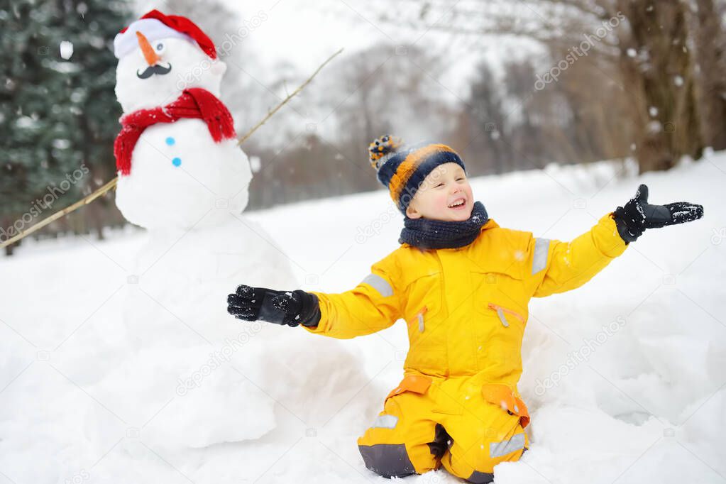 Little boy playing with funny snowman. Active outdoors leisure with children in winter.