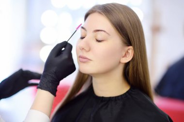 Beautician yüz genç güzel model üzerinde özel fırça kullanarak kaşları tarar. Yüz bakımı ve makyaj