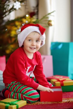 Evdeki köknar ağacının altında Noel hediyesi olan şirin bir çocuk. Noel sabahı mutlu bir çocuğun portresi.