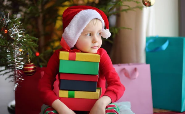 Cute little boy with a Christmas gift under fir tree at home. Portrait of frustrated kid in Christmas morning. Stock Photo