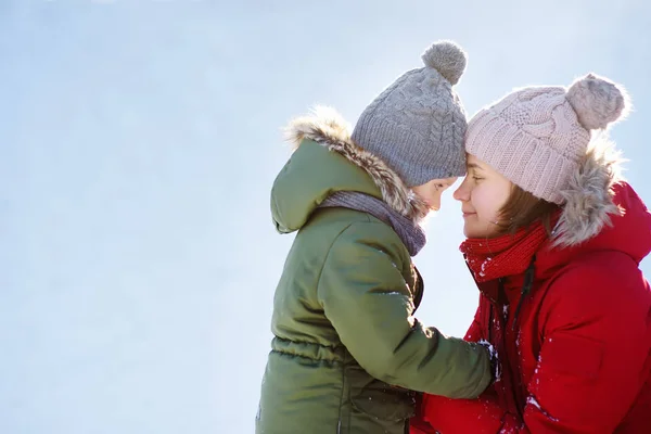 若い母親と彼女の小さな息子は、一緒に雪の冬の公園を散歩中に抱擁し、楽しんでいます — ストック写真