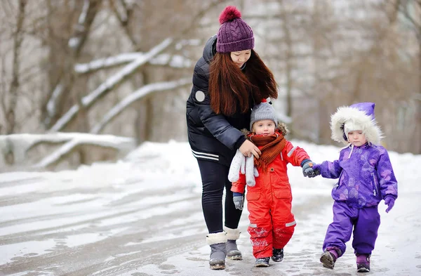 Young asian woman helping caucasian toddler boy anf girl with their winter clothes — Stock Photo, Image