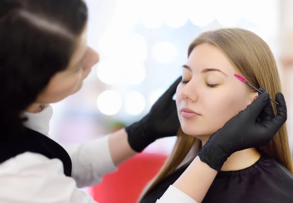 Kosmetikerin kämmt Augenbrauen mit speziellen Pinsel auf Gesicht junge schöne Modell. Gesichtspflege und Make-up — Stockfoto