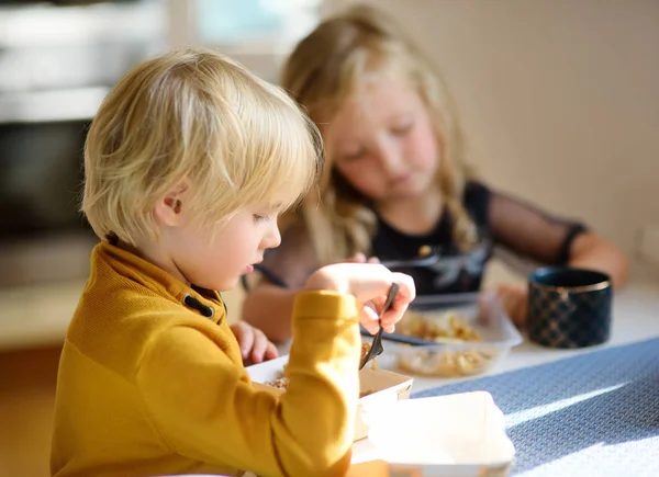 Pré-escolares está comendo alimentos rápidos ou de conveniência na cozinha em casa. Nutrição de uma família moderna em uma cidade grande. Serviços de distribuição de alimentos . — Fotografia de Stock