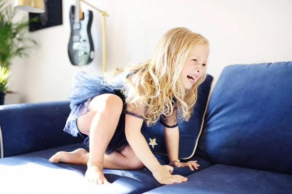 Mischievous kleuter meisje springen op een bank. Actieve spelletjes voor kind thuis. — Stockfoto