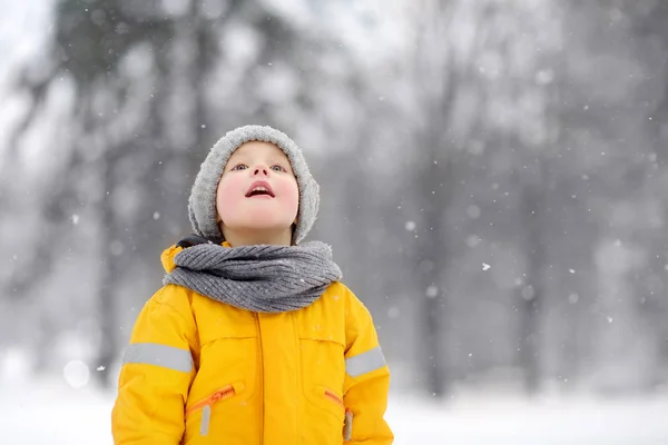Meglepett kisfiú sárga téli ruhában sétál hóesés közben.. — Stock Fotó