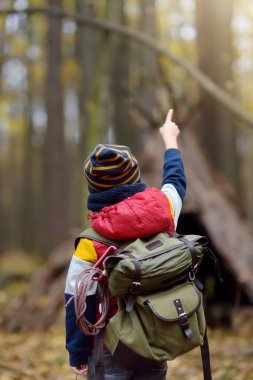Sonbahar ormanlarında yürüyüş yaparken dürbünlü küçük bir izci. Arka planda çadır kulübesi.