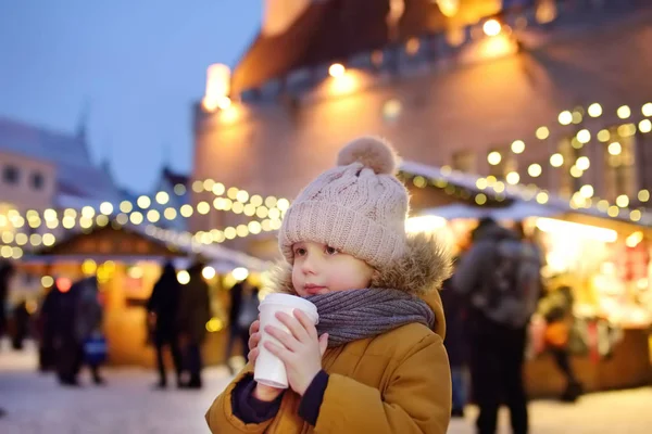 A kisfiú forró csokit vagy forralt bort iszik a karácsonyi piacon Tallinnban, Észtországban.. — Stock Fotó