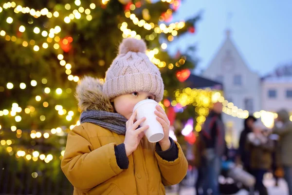 Niño pequeño está bebiendo chocolate caliente o vino caliente niño cerca de gigantes abeto de Navidad . — Foto de Stock