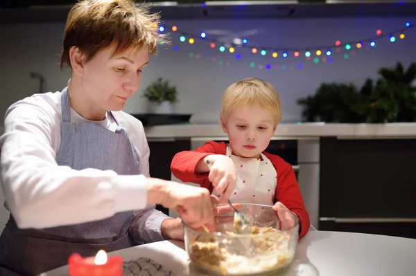 在节日期间，快乐的小男孩和他年轻的祖母一起烘焙饼干。 圣诞节和有孩子的新年. — 图库照片