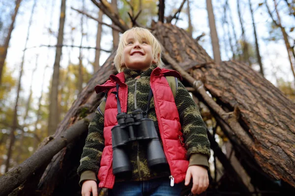 Niño explorador con binoculares durante el senderismo en el bosque de otoño. Cabaña de tipi en el fondo . —  Fotos de Stock