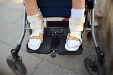 Tekerlekli sandalyede oturan engelli kız. Bacakları ortoza dönmüş. Fotoğrafı kapat. Çocuk serebral felci. Engelli. Katılım. Engelli çocuklu aile.