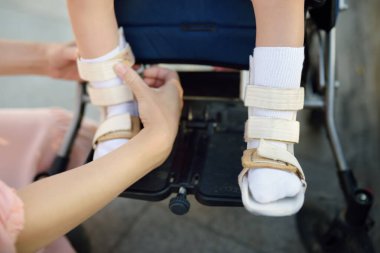 Anne kızına ortopedik bacak takıyor. Tekerlekli sandalyede oturan engelli kız. Çocuk serebral felci. Engelli. Rehabilitasyon aracı. Katılım. Engelli çocuklu aile.