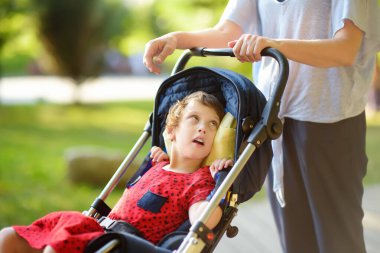 Parkta tekerlekli sandalyeli engelli bir kızla yürüyen bir kadın. Çocuk serebral felci. Engelli. Rehabilitasyon aracı. Ortopedi. Katılım. Engelli çocuklu aile.