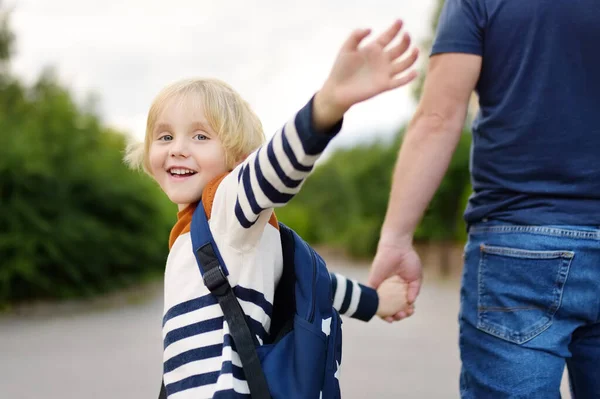 Little boy with his father going to school after summer break. Education for little kids. Back to school concept. Schoolboy turns and waves goodbye