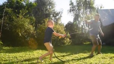 Küçük komik bir çocuk ve babası güneşli arka bahçede bahçe hortumuyla oynuyorlar. Anaokulu çocuğu su püskürterek eğleniyor. Çocuklu aile için yaz etkinliği.