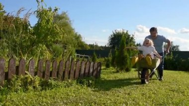 Sıcak, güneşli bir günde evin bahçesinde babasının arabasıyla gezen mutlu küçük çocuk. Hasat zamanı arka bahçede çocukları olan aile için açık hava oyunları.