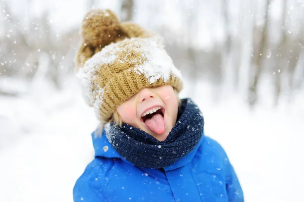 Petit garçon drôle en vêtements d'hiver bleu marche pendant une chute de neige. Activités d'hiver en plein air pour les enfants — Photo