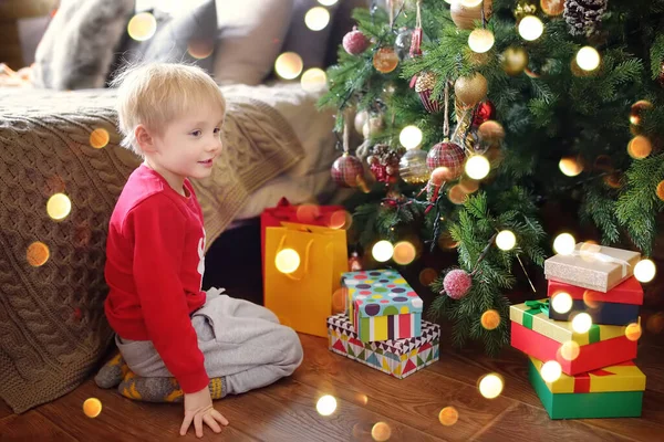 Petit garçon endormi avec un cadeau de Noël sous sapin à la maison. Portrait d'enfant heureux le matin de Noël — Photo