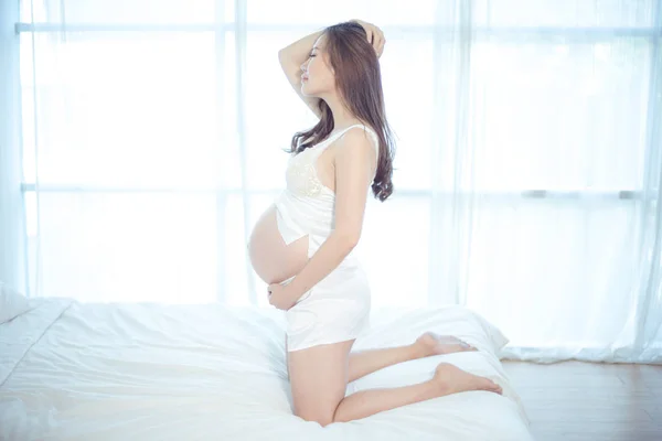 迷人的怀孕亚洲妇女在床上 抱着她的肚子 — 图库照片