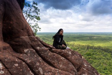 Genç bir kadın dağın tepesinde oturuyor.