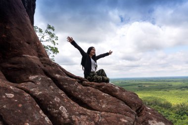 Genç bir kadın dağın tepesinde oturuyor.