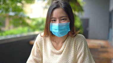 Yeşil ağaçta yüz maskesi takan Asyalı genç bir kadının portresi