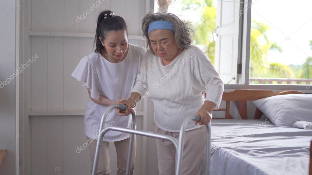 Asian adult woman or daughter support senior mother use walker at home