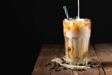 Krem üzerine dökülür ve bir eski rustik ahşap masa üzerinde kahve çekirdekleri ile uzun bir bardak buzlu kahve. Koyu ahşap arka plan kopya alanı ile soğuk yaz içki.