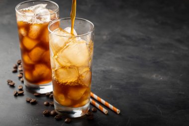 Buzlu kahve üzerinden uzun bir cam ve kahve çekirdekleri bir eski rustik ahşap tablo. Kopya alanı ile karanlık bir arka plan üzerinde soğuk yaz içeceği. Bir bardak içine bir kahve kabı üzerinden dökülen içki süreci.