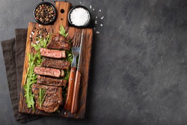 Closeup biftek new York sığır ırkları kara Angus otlar, sarımsak ve ahşap bir tahta üzerine tereyağı ile yemeye hazır. Bitmiş çanak taş karanlık bir arka plan akşam yemeği için. Kopya alanı ile Üstten Görünüm