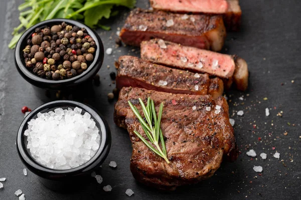 Primer plano listo para comer carne de res de Nueva York razas de negro Angus con hierbas, ajo y mantequilla en una tabla de piedra. El plato terminado para la cena sobre un fondo de piedra oscura. Vista superior —  Fotos de Stock